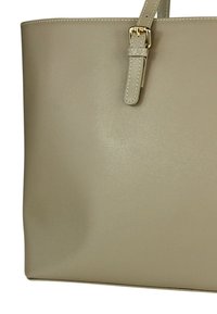 Beige draagtas van gestructureerd synthetisch materiaal, met een gespband en strakke lijnen voor een gestructureerde uitstraling.