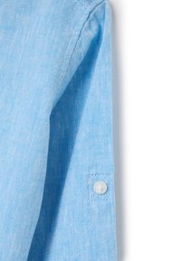 Manga de camisa de lino azul claro con corte recto, que presenta un detalle de botón en el puño y un acabado ligeramente texturizado.