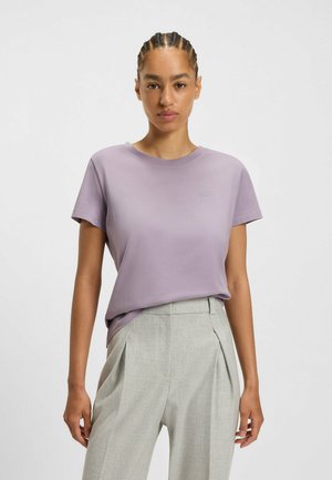 Helllila kurzärmliges T-Shirt mit Rundhalsausschnitt und kleinem gestickten Logo, kombiniert mit hellgrauen, maßgeschneiderten Stoffhosen. Glatte Textur.
