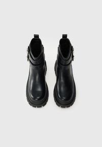 Pair of black leather ankle boots with chunky soles and double silver buckle straps on a white background.