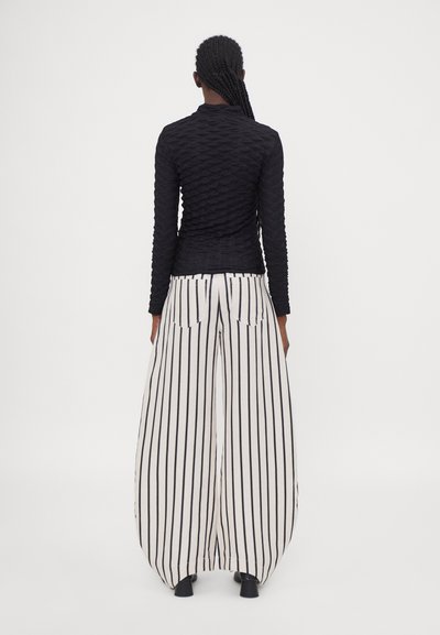 Black textured long-sleeve top paired with wide-leg white pants featuring black vertical stripes and back pockets.