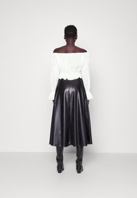 Top bianco a spalle scoperte con maniche a palloncino, abbinato a una gonna midi nera in pelle sintetica che si allarghera' all'orlo. Stivaletti neri aderenti completano il look.