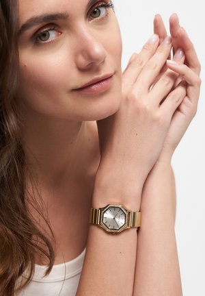 Gold octagonal wristwatch with a silver dial, featuring a textured, polished finish, and a crystal-accented bezel on a metallic bracelet.