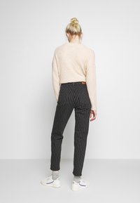 Ljusrosa texturerad stickad tröja och svarta randiga byxor med bakfickor, ihop med vita sneakers och grå strumpor.