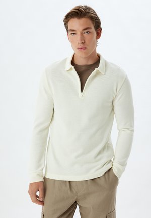 Langärmliger Polo-Sweatshirt in hellgelb, mit einem halbseitigen Reißverschlusskragen, strukturiertem Stoff und enganliegenden Bündchen, kombiniert mit beigen Hosen.