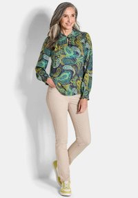 Bunt gemusterte Paisley-Bluse mit langen Ärmeln und knöpfbarem Kragen; kombiniert mit beigen Hosen und Sneakers mit gelben Akzenten. Weicher Stoff.