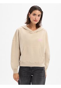 Beige capuchontrui met een voorzak, geribbelde boorden en onderzoom. Heeft een roze logo op de borst en een relaxte pasvorm.