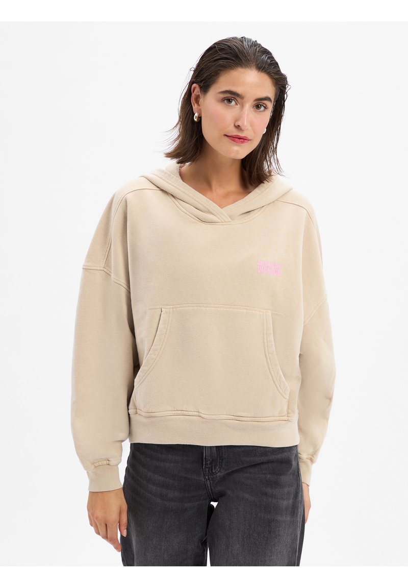 Beige capuchontrui met een voorzak, geribbelde boorden en onderzoom. Heeft een roze logo op de borst en een relaxte pasvorm.