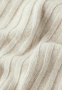 Cremefarvet strikket stof med et struktureret diagonalt ribmønster, som har bløde fibre og synlige syninger overalt.