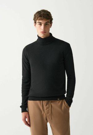Pulover negru cu guler înalt dintr-un material tricotat moale, având mâneci lungi și un design ajustat, asortat cu pantaloni maro deschis.