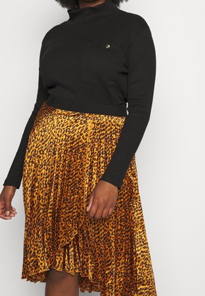 Vrouw draagt een zwart topje met lange mouwen en een zak, gecombineerd met een geplooide rok met een oranje-zwart luipaardprint.