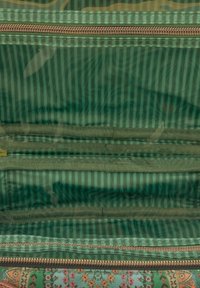 Groen gestreepte stoffen binnenkant van een tas met verschillende rits- en elastische vakken zichtbaar.