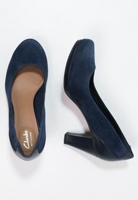 Námořnické modré semišové lodičky na vysokém podpatku s kulatou špičkou, polstrovanou stélkou a kontrastním černým lesklým podpatkem. Hladký povrch s klasickým designem.