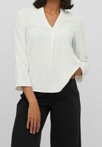 Blouse blanche texturée avec un col en V et des manches trois-quarts, associée à un pantalon noir à jambes larges. Design simple et contemporain.