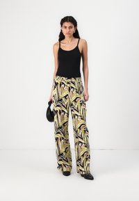 Black sleeveless top with fitted design paired with wide-leg trousers featuring a colorful leaf pattern in green, beige, and black.