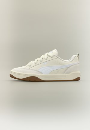 Kremfarvet sneakers med lavt skaft, hvid side-stribe, snørelukning foran, polstret krave og brun gummisål på neutral baggrund.