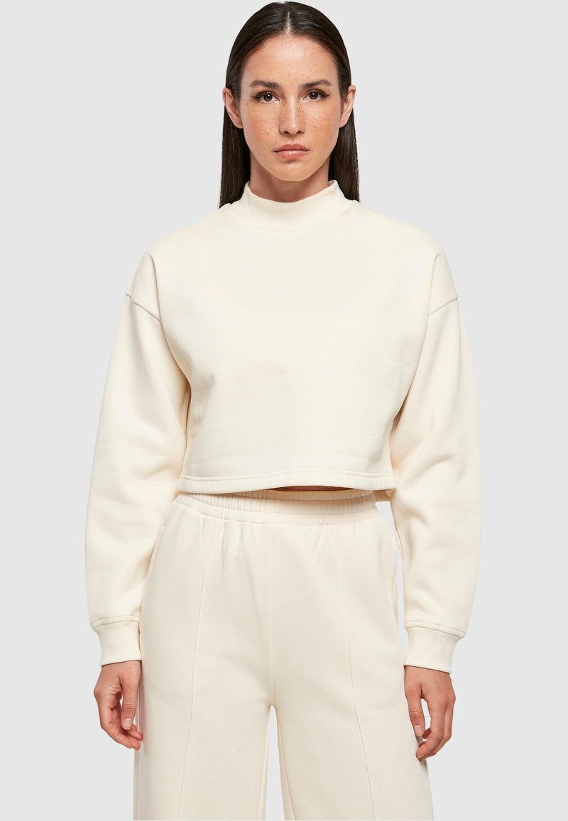 Lühendatud, kreemivärvi pusakleit pehmest kangast, millel on kõrge krae ja pikad varrukad. Sile pind ilma nähtavate mustriteta.