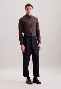 Bruine blouse met lange mouwen en kraag, met knoopsluiting, gecombineerd met marineblauwe wijde broek en zwarte veterschoenen.