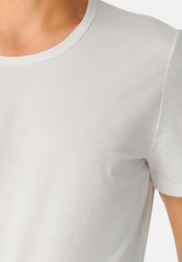 T-shirt blanc à manches courtes avec un col rond et des rayures verticales subtiles, fabriqué en tissu doux et lisse. Pas de logos ou graphiques visibles.