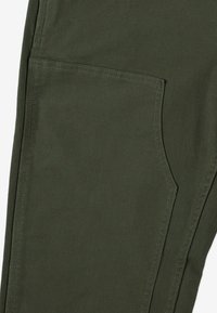 Zbliżenie na oliwkowozielone spodnie z tkaniny, pokazujące dużą boczną kieszeń z podwójnym szwem.