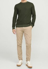 Pull en tricot vert foncé avec ourlet côtelé et manches longues, associé à un pantalon beige clair ajusté et des baskets blanches.