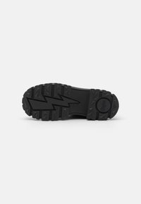 Suela de bota de goma negra con un diseño de banda de rodadura texturizado y antideslizante que presenta patrones triangulares y acentos en forma de rayo. Logo circular en el talón.