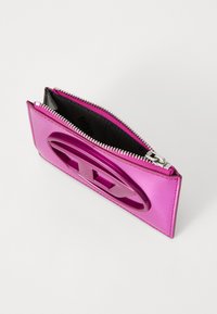 Pink patent leather wallet with a glossy surface, zip closure, and a large cut-out logo accent on the front. Interior is black fabric.