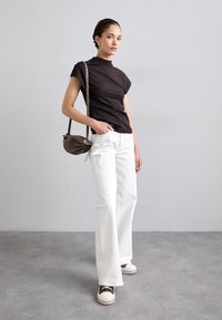 Top negru ajustat, pantaloni albi evazați și geantă maro. Prezintă mâneci scurte, țesătură fină și o siluetă relaxată. Tenisi maro și albi.