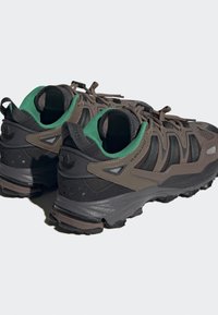 Chaussures de trail en marron foncé et noir avec des accents verts ; présentent une tige texturée, un col rembourré et une semelle extérieure robuste pour une traction optimale.