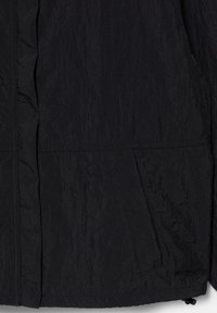 Gros plan d’un tissu noir texturé avec des lignes de couture visibles et une poche à rabat sur le côté droit.