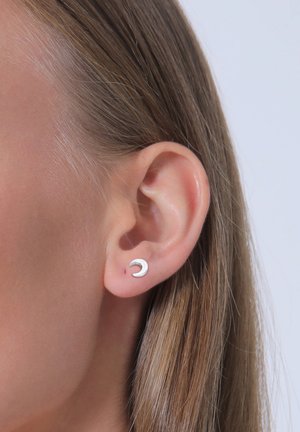 Silberner, mondförmiger Ohrring, der in einer Nahaufnahme des Ohrs gezeigt wird, mit glatter Oberfläche und minimalistischem Design.