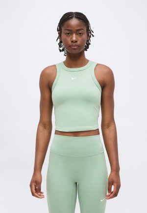 Jonge vrouw met gevlochten haar, een lichtgroen mouwloos crop top en bijpassende hoge taille leggings, beide met kleine witte Nike-logo's.