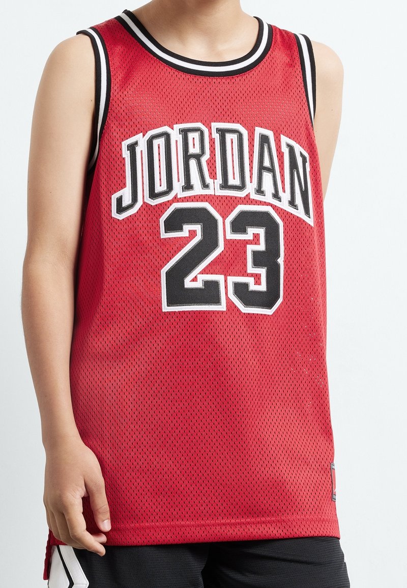 Personne portant un maillot de basket-ball rouge sans manches avec "JORDAN" et le numéro 23 en lettres noires et blanches en gras, montrée des épaules aux cuisses.