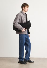 Sort, struktureret håndtaske holdt under armen, parret med en tekstureret grå velourjakke og løse blå denimjeans, afsluttet med sorte sko.