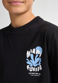 Camiseta de algodón negra con un gráfico colorido que presenta "Miami" y "Florida" en blanco y azul claro, con cuello redondo.