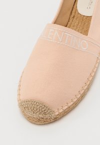 Espadrile din pânză de culoare roz deschis, cu talpă din sfoară de iută. Prezintă o bandă cu logo cusută și o textură netedă.
