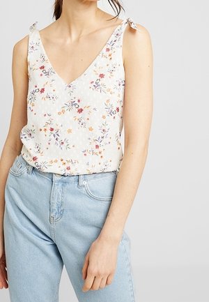 Haut blanc sans manches à petit imprimé floral avec des bretelles nouées aux épaules, porté avec un jean taille haute bleu clair.