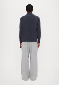 Marineblaues Langarmhemd mit lockerer Passform, weichem Stoff und Kentkragen, kombiniert mit hellgrauen, weit geschnittenen Hosen aus leichtem Material.