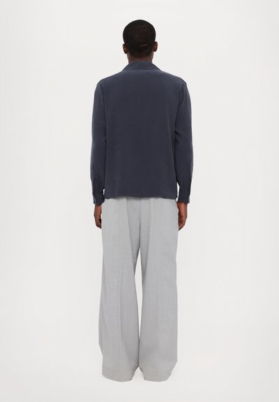 Camisa de manga larga en color navy con un corte relajado, textura suave y cuello de solapa, combinada con pantalones de pierna ancha en gris claro de un tejido ligero.