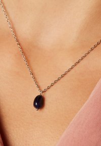 Zilveren ketting met een ovale donkerblauwe hanger. Hanger heeft een gladde oppervlakte en is bevestigd met een eenvoudige zilveren bail. Minimalistisch ontwerp.