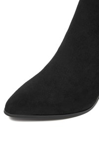 Czarne zamszowe botki do kostki z ostrym noskiem i smukłym designem; mają gładką teksturę i cienką czarną podeszwę.