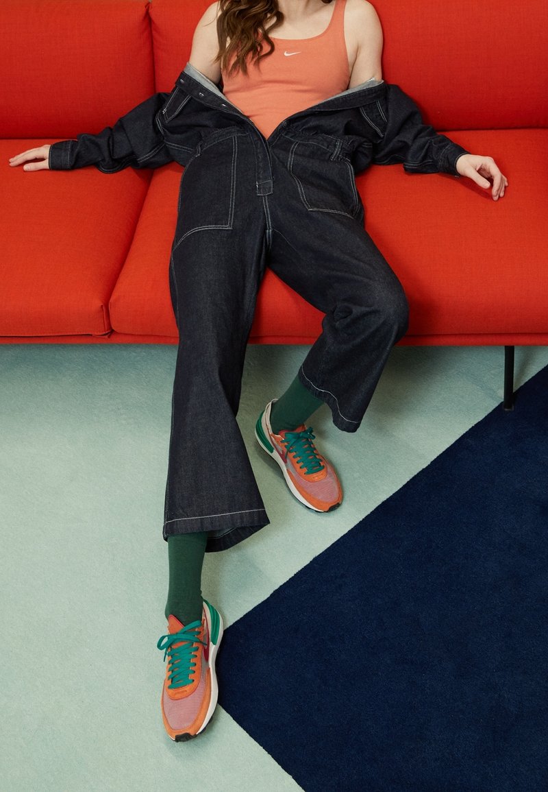 Jeansjacka och löst sittande mörka jeans, kombinerat med en orange linne, gröna strumpor och färgglada sneakers på en röd soffa.