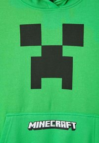 Felpa verde brillante con un grande volto di Creeper pixelato nero e la parola "Minecraft" in lettere a blocchi sulla tasca frontale.