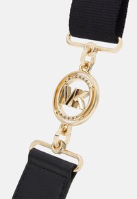 Cinturino in pelle nera con hardware dorato. Presenta un logo circolare con la scritta "Michael Kors" e un attacco a catena massiccia.