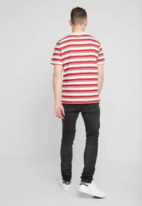 Camiseta de manga corta a rayas rojas y blancas, material de algodón, ajuste relajado, combinada con pantalones vaqueros negros y zapatillas blancas sobre un fondo simple.