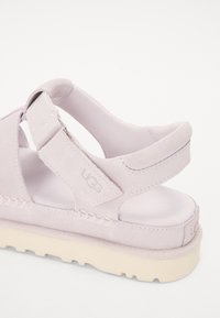 Vaaleanpunaiset mokkasandaalit, joissa on pehmeä pinta, säädettävät hihnat ja pehmustettu pohja, suunniteltu mukavuutta ja tukea varten.