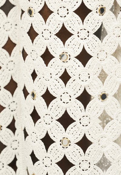 Tissu blanc en crochet avec motifs floraux en forme de losange et petits accents circulaires réfléchissants bordés d'or sur fond sombre.