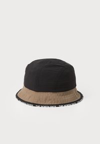 Zwarte en beige stoffen bucket hat, voorzien van een gestikt ontwerp en een gebrandmerkte zwarte band met witte letters rondom de rand.