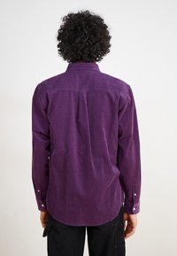 Paarse corduroy shirt met lange mouwen, knoopsluitingen aan de manchetten en een achterste plooi voor bewegingsgemak. Gladde textuur en casual ontwerp.