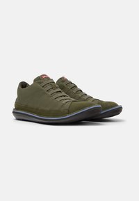 Olive green canvas sneakers with textured material, rounded toe, and black rubber sole featuring a blue accent along the edge.